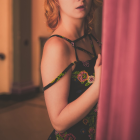 Red-haired woman in floral black dress behind curtain, gazing sideways