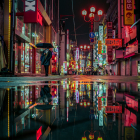 Person with umbrella on wet city street at night with vibrant lights and reflections