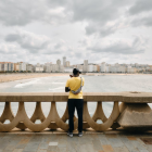 Person in yellow shirt and hat by river with bridge and cloudy sky