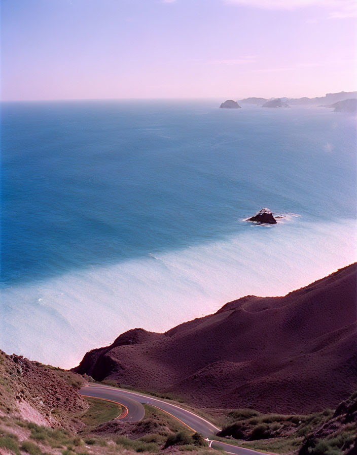 Scenic coastal road descending mountain slope by serene ocean and distant islet