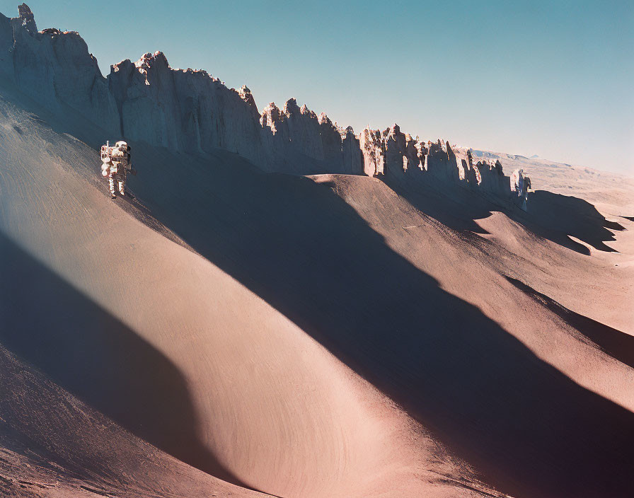 Astronaut on Sandy Slope with Jagged Rock Formations