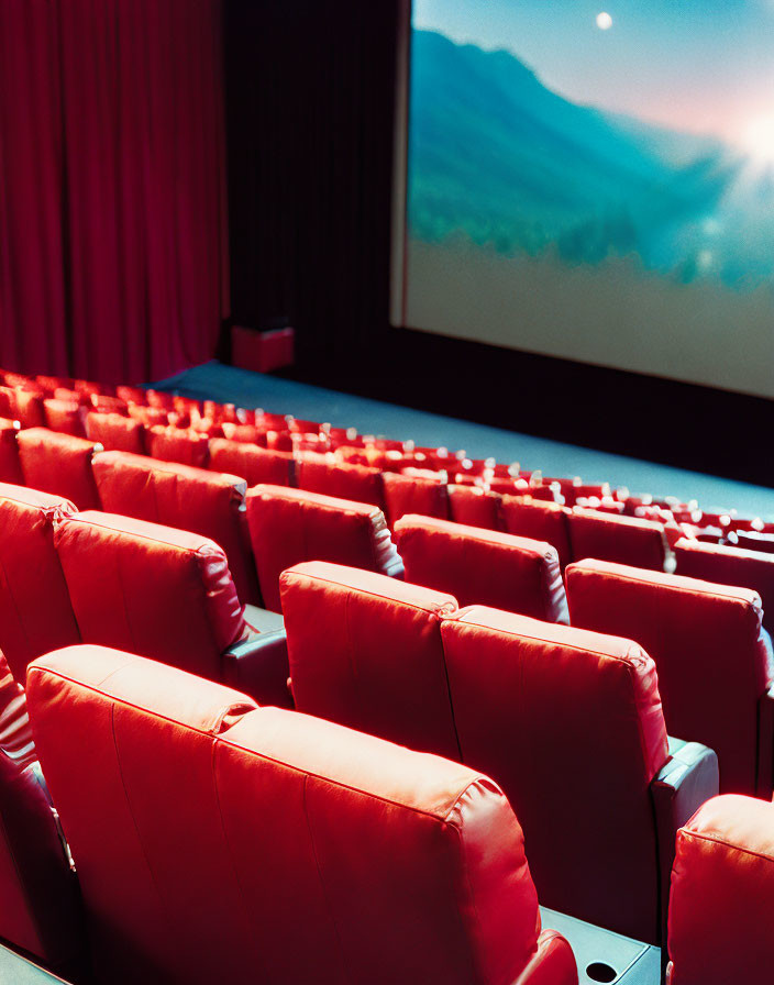 Red cinema seats facing mountain view on large screen in dimly lit theater