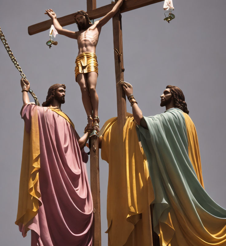 Religious statues depicting crucifixion scene with figures in robes against clear sky