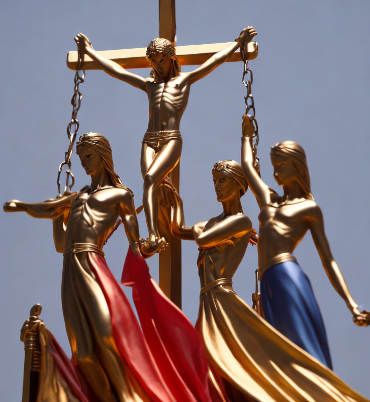 Golden Jesus statue on cross with four figures in flowing robes under clear blue sky