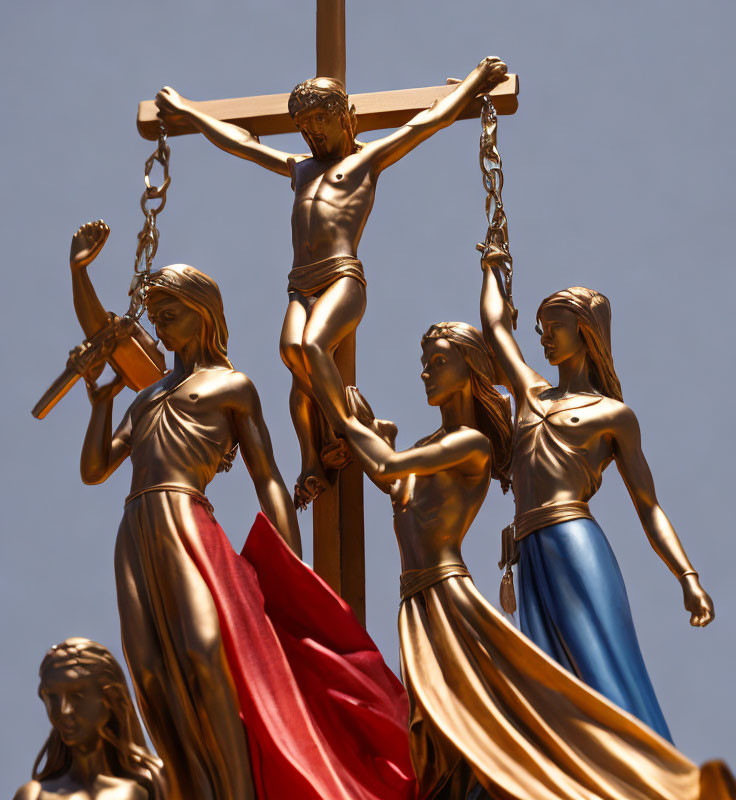 Religious sculpture of Jesus on cross with female figures under blue sky