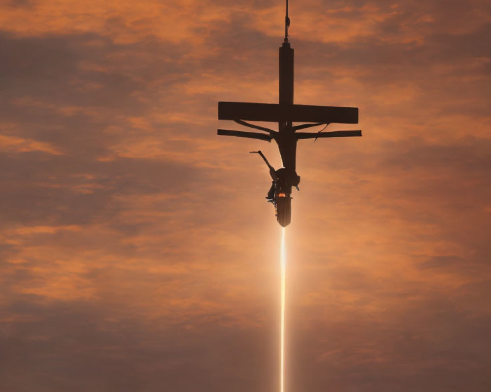 Person hanging from cross-like structure under bright sun against orange sky