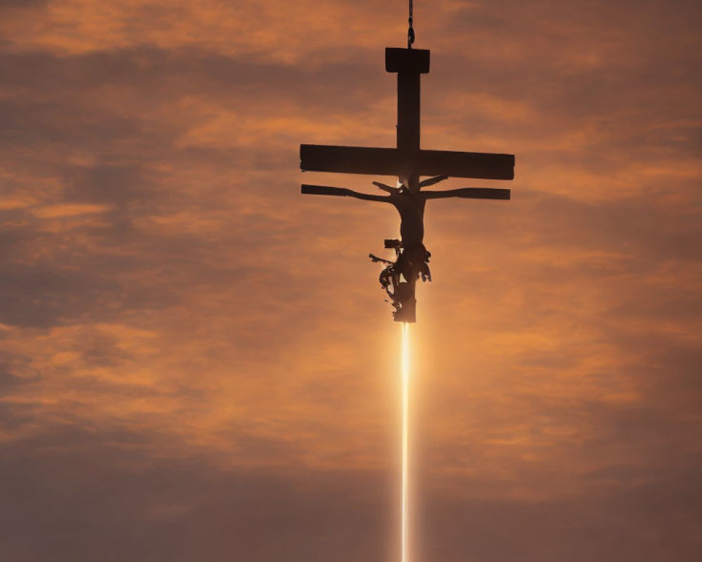 Silhouette of crucifix and figure under cloudy sunset sky with vertical light ray