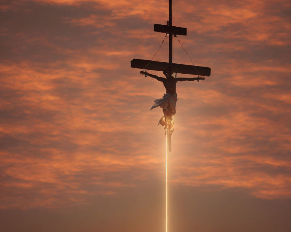 Silhouette of crucifix at sunset with orange clouds and sun rays