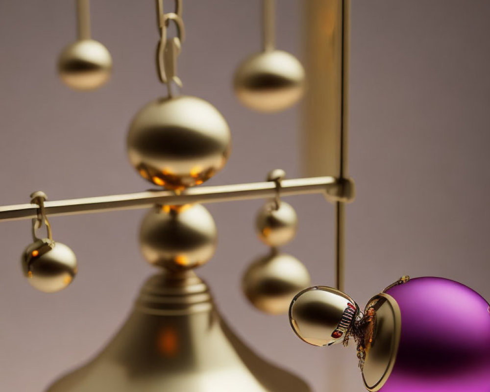 Elegant kinetic mobile with golden and purple spheres, featuring a toppled purple ball on a chain