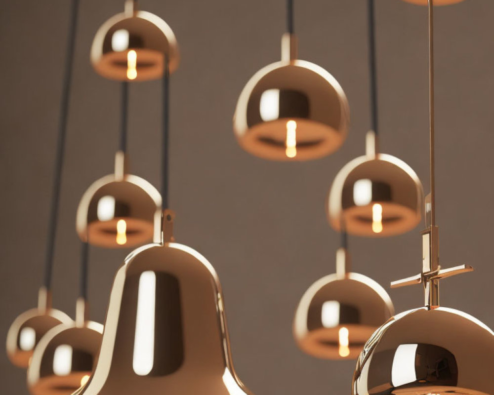 Reflective brass pendant lights in various heights on neutral background