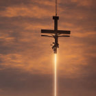 Person hanging from cross-like structure under bright sun against orange sky