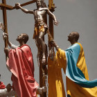 People in colorful robes carrying a cross statue in religious procession.