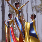 Three female figures in blue and yellow gowns with red capes, dancing in a forest