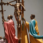 Religious statue of Jesus on the cross with two figures in colorful robes