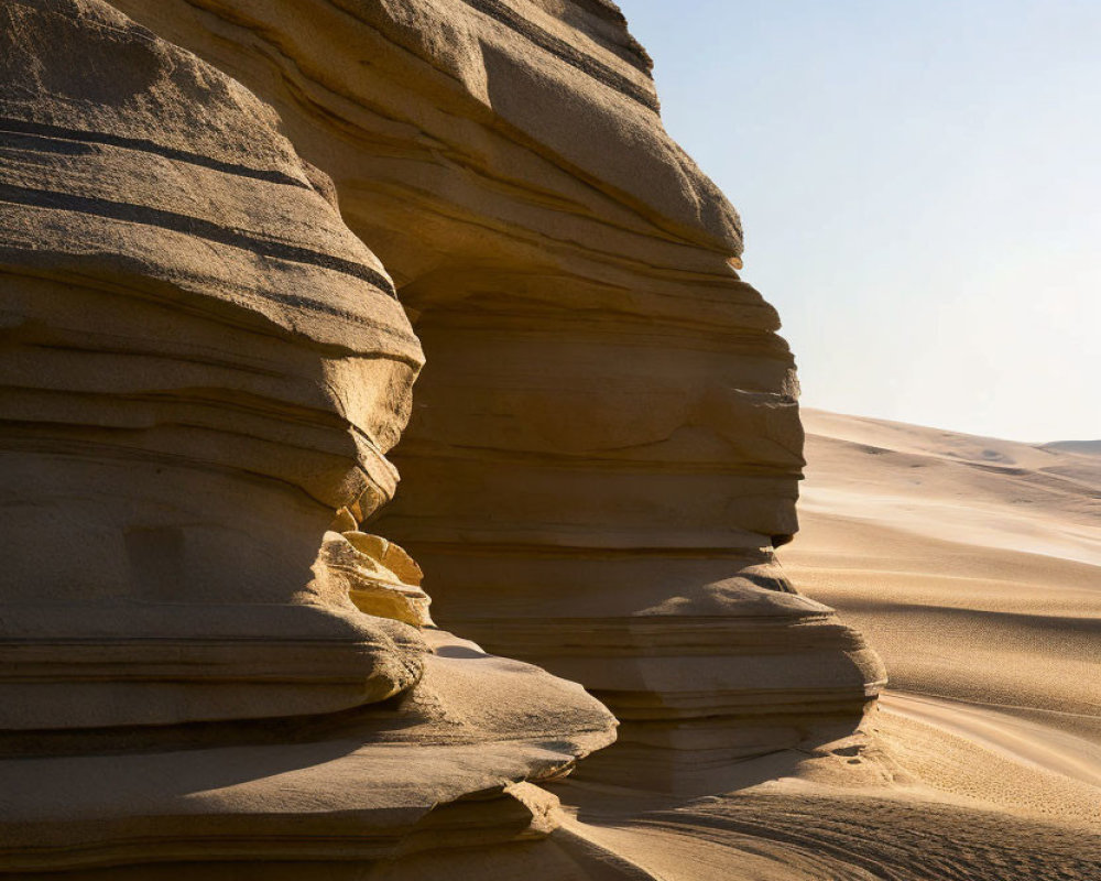 Sand dunes and layered rock formation under clear sky at golden hour