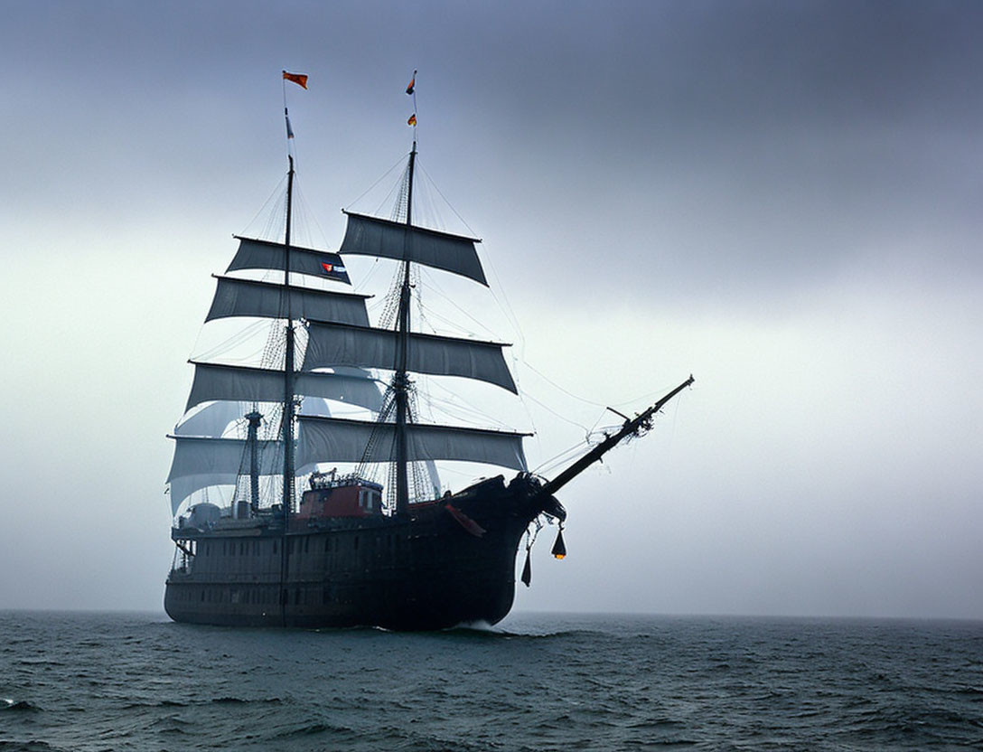 Tall ship with multiple sails on calm sea under overcast sky