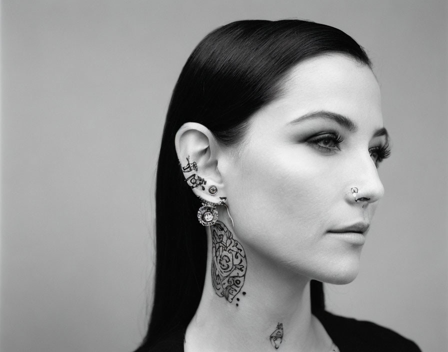 Monochrome profile of woman with distinctive piercings, eyeliner, and neck tattoos