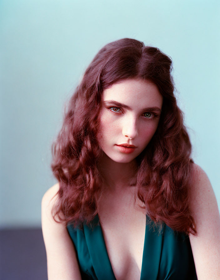 Young woman with wavy brown hair and green eyes in green top on blue background