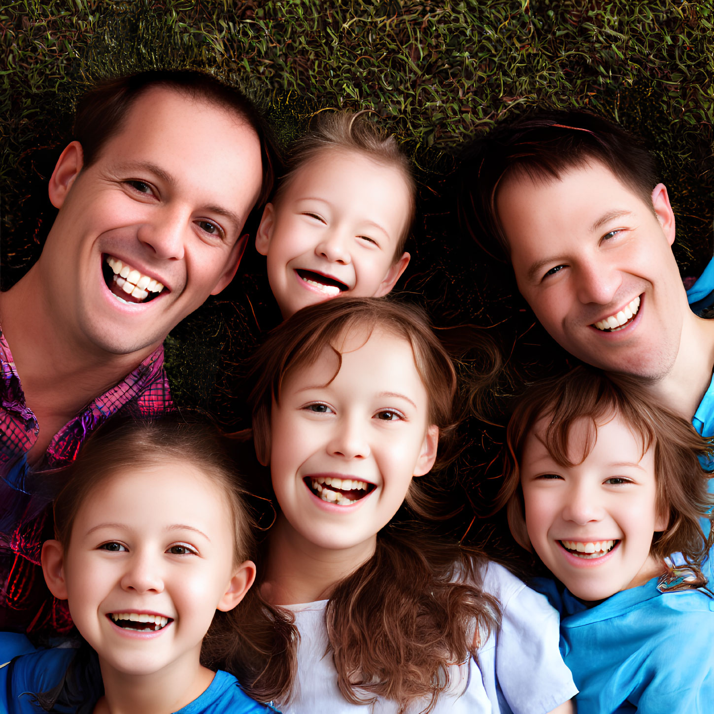 Happy family of two adult males and three young girls lying on grass outdoors