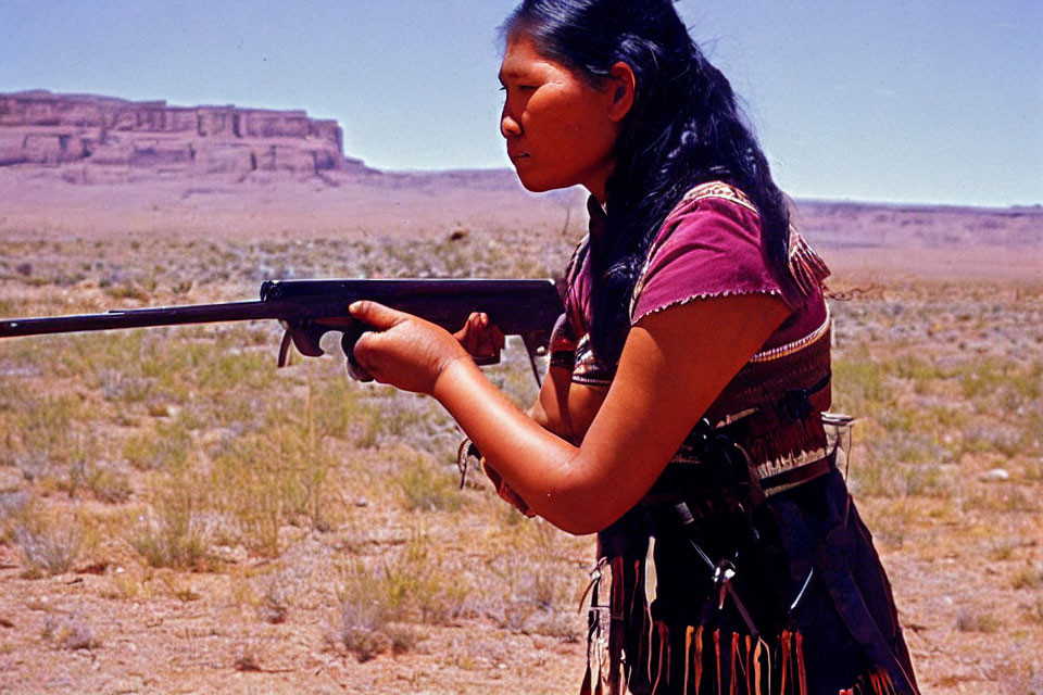 Traditional attire woman aiming rifle in desert with mesa.