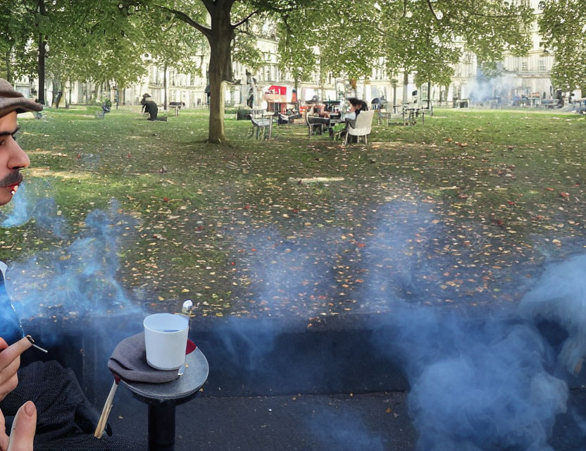 Person exhaling smoke in park with coffee cup and autumn leaves.