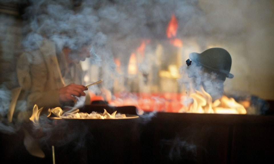 Person in Hat Cooking Over Open Flame Surrounded by Smoke