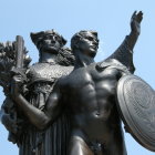 Three metallic female warrior statues with intricate armor and wing-like adornments on blue background