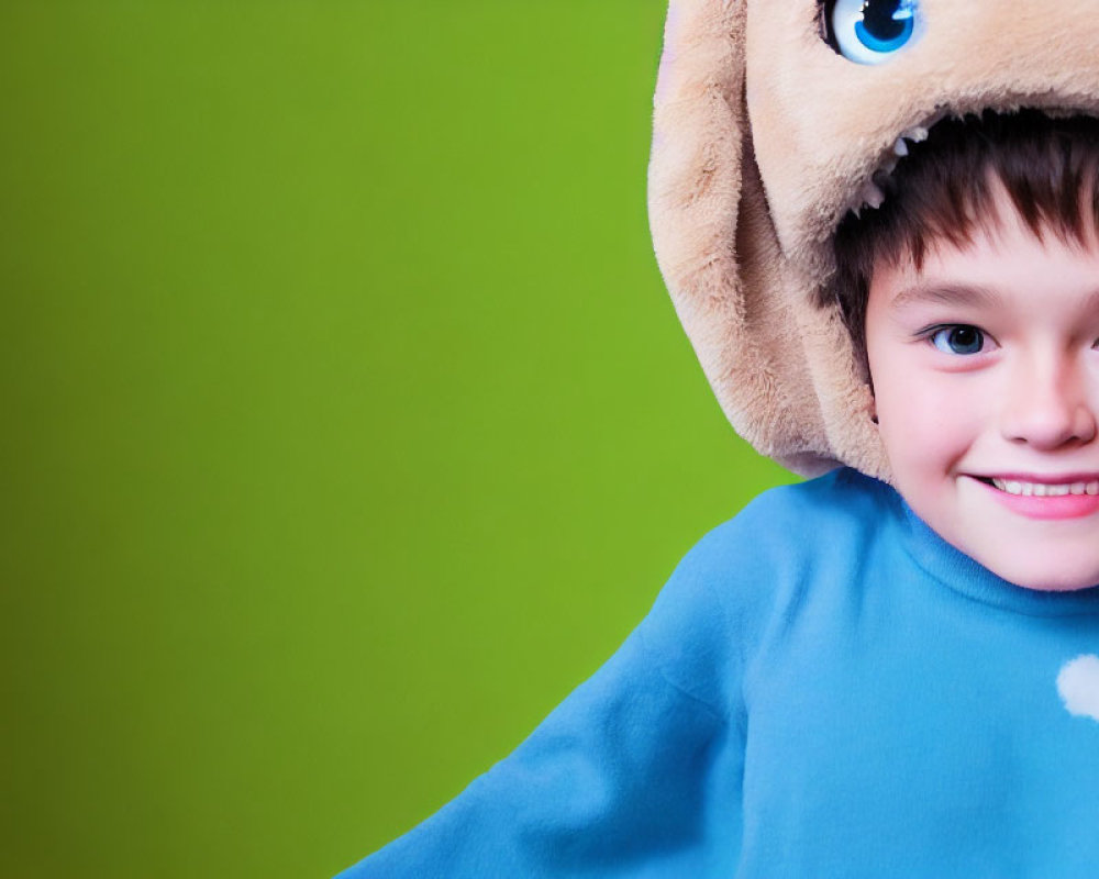 Child in Blue Shirt Wearing Bear Hat on Green Background