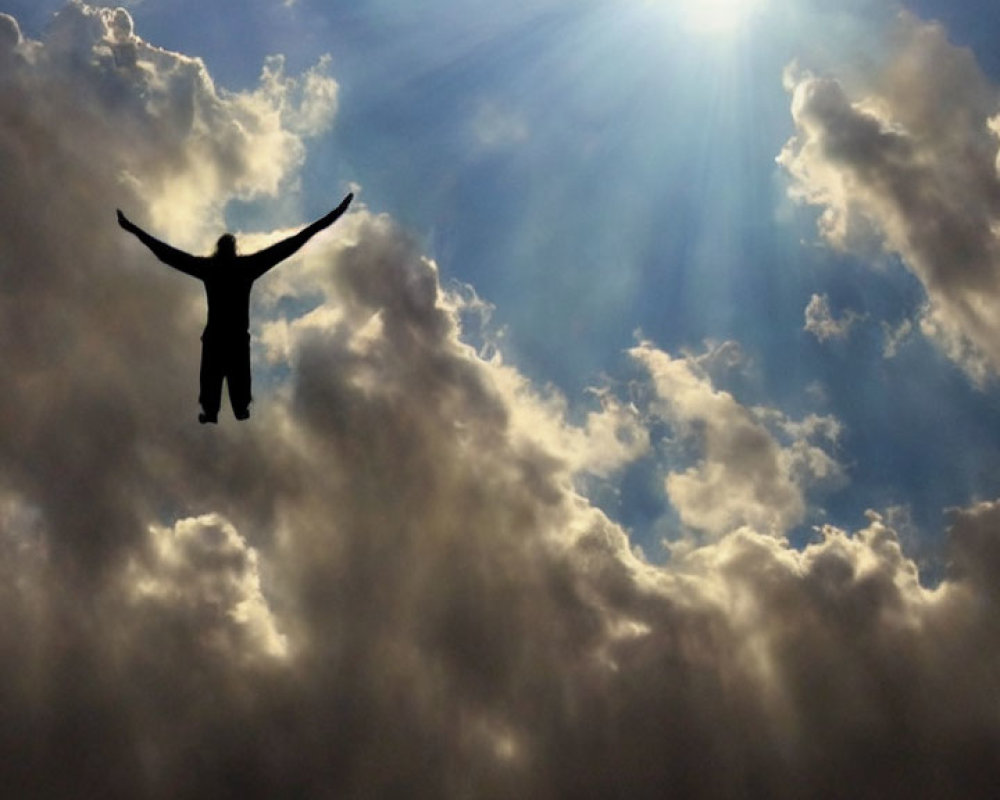 Person's silhouette with raised arms under dramatic sky with sunbeams.