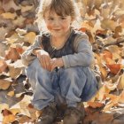 Child in denim overalls among pumpkins and fallen leaves in sunlight