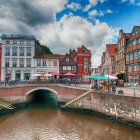 Vibrant village painting with colorful houses, flowers, canal, and bridges under blue sky