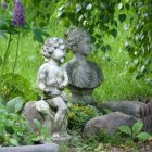 Cherubic statues with floral crowns on stone bench in lush garden