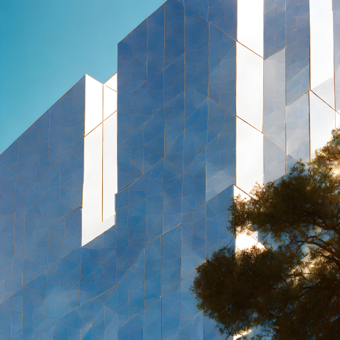 Modern building with geometric facade and tree against clear blue sky