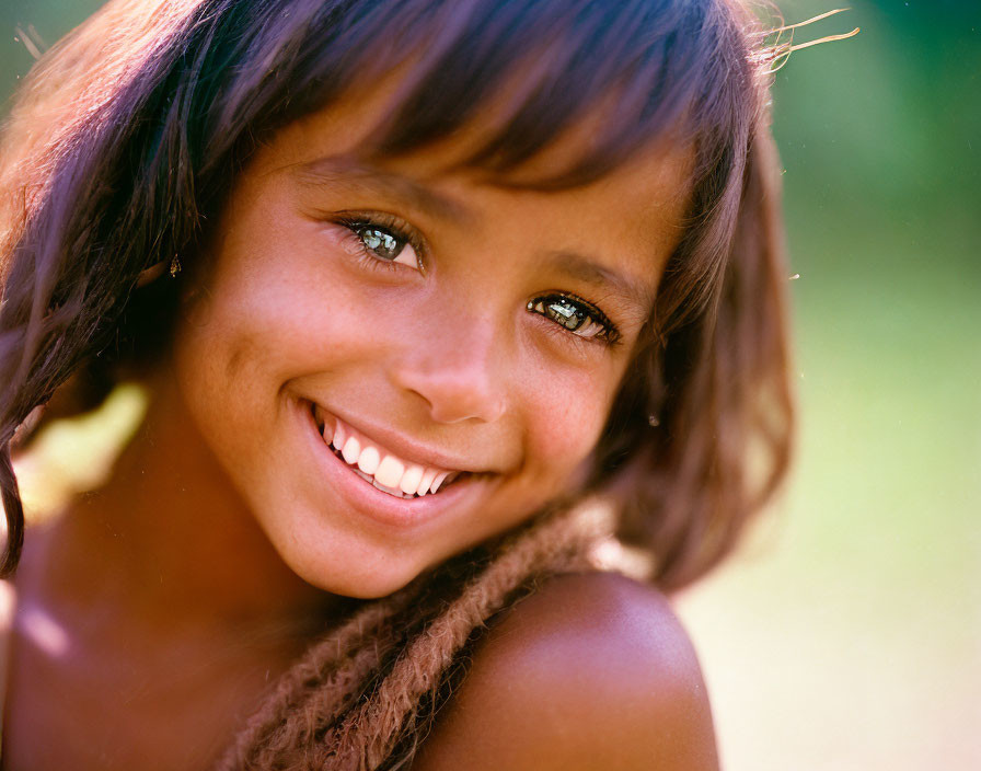 Smiling young girl with sparkling eyes and long brown hair in natural light