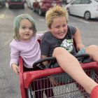 Woman with creepy doll in shopping cart, eerie makeup, small dog, vintage cars.