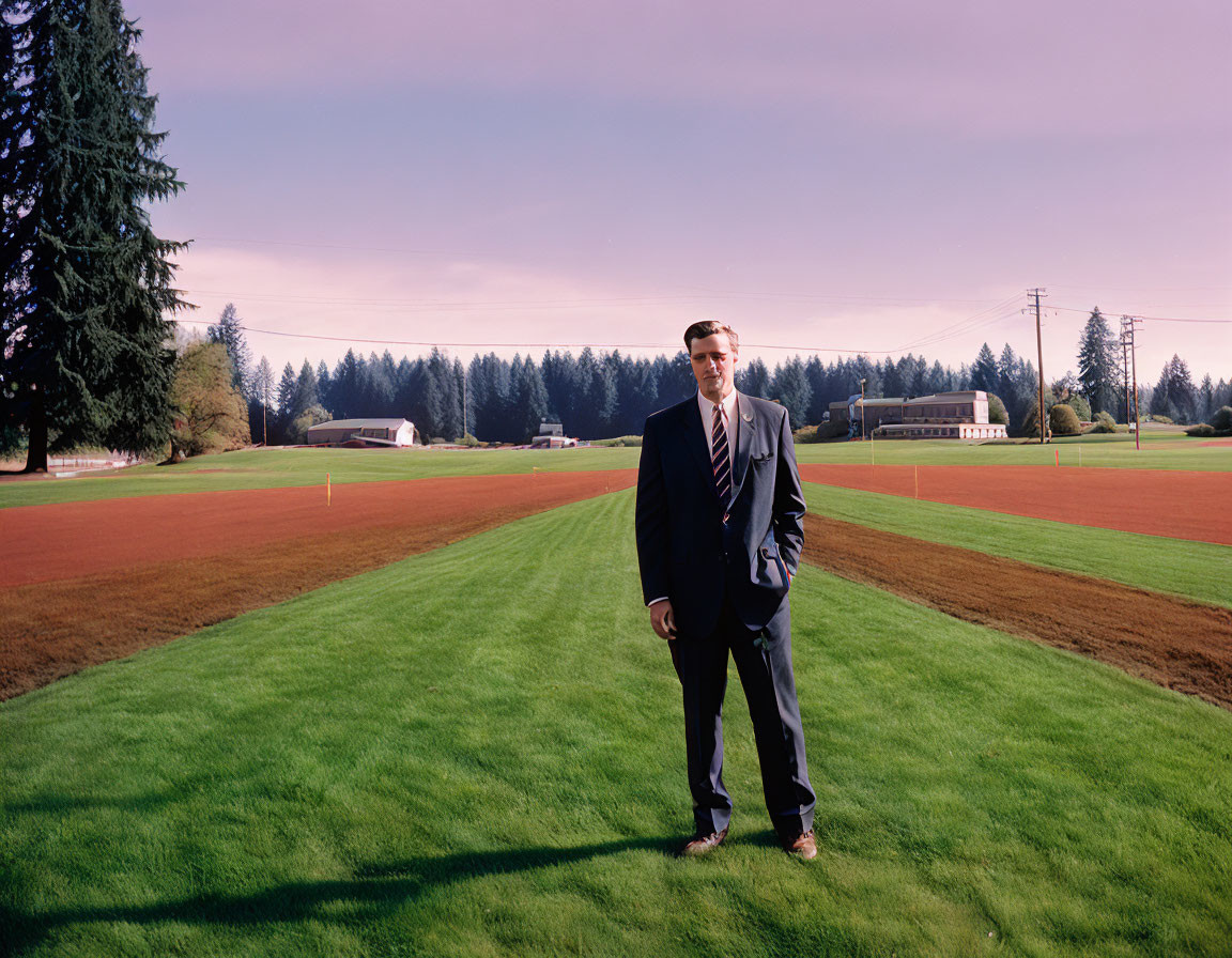 Businessman in suit and sunglasses on manicured field with trees and clear sky