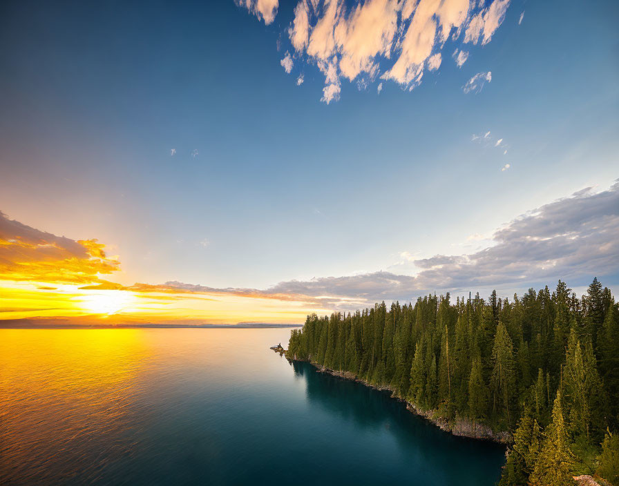 Tranquil lake sunset with forested peninsula and scattered clouds