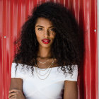 Dark-haired woman in golden jewelry and white top against red and white backdrop