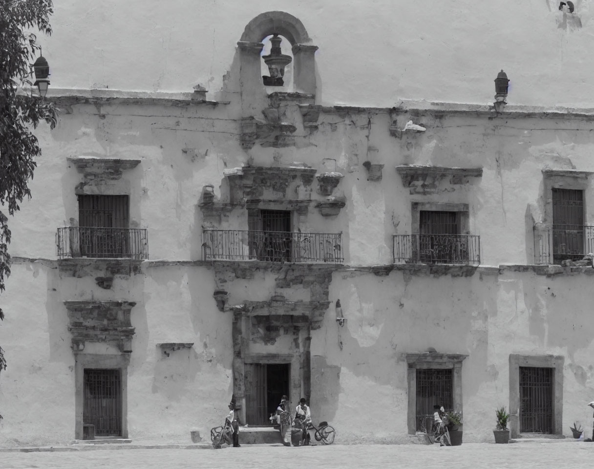 White Building with Two Balconies and Arched Doorway, People with Bicycles in Front