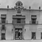 White Building with Two Balconies and Arched Doorway, People with Bicycles in Front