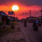 Traditional village at dusk: Misty houses, fiery sky, glowing moon