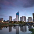 Colorful futuristic cityscape reflected in calm water under a dusk sky