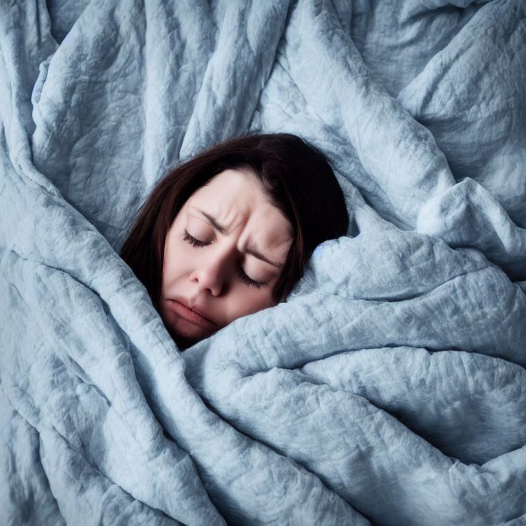 Person wrapped in blue-grey blanket with pained expression.