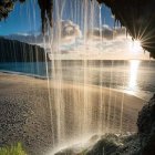 Natural arch framing waterfall, beach, and sea under clear sky