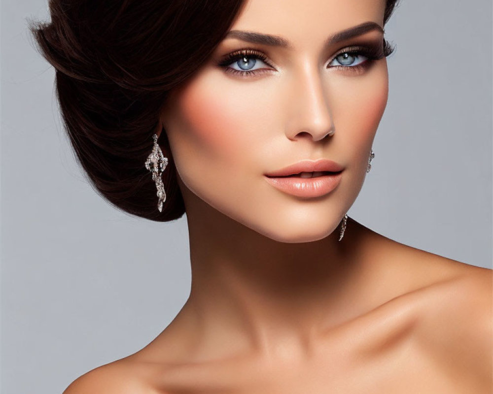 Sophisticated updo hairstyle, blue eyes, diamond earrings on woman against gray background