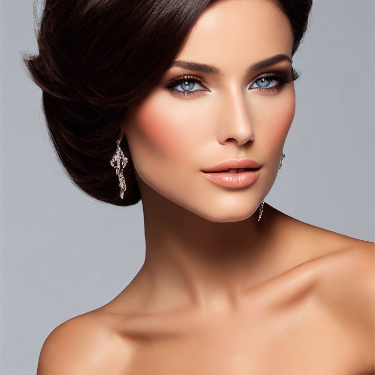 Sophisticated updo hairstyle, blue eyes, diamond earrings on woman against gray background