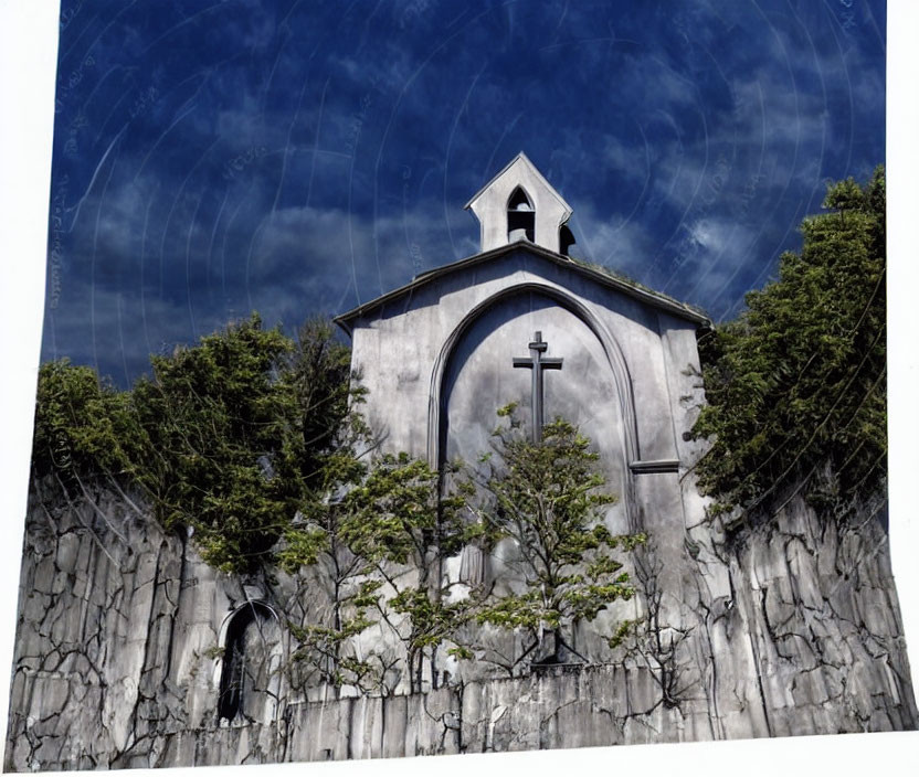 White facade church with cross, stone wall, greenery, blue sky.