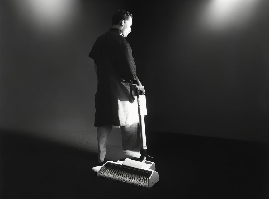 Man in dark outfit with vacuum cleaner on dimly lit stage