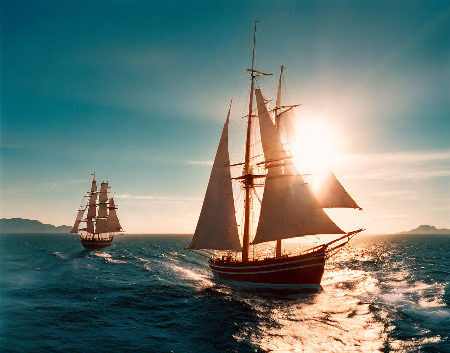 Tall ships sailing at sunset with sun rays on ocean horizon