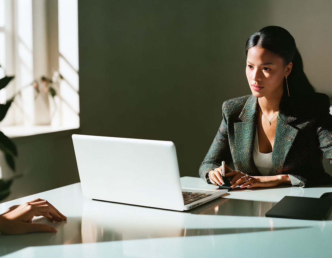 Woman at desk taking notes with person's hand gesturing nearby